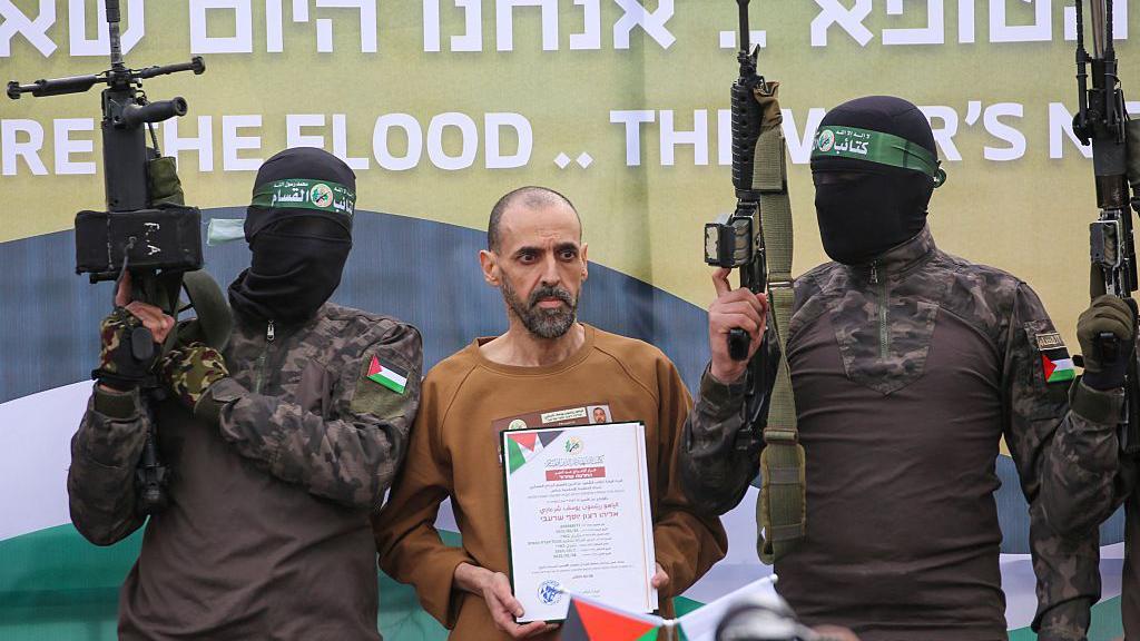 Naoružani borci Hamasa sa maskama na licima i izraelski taoc Elij Šarabi na bini