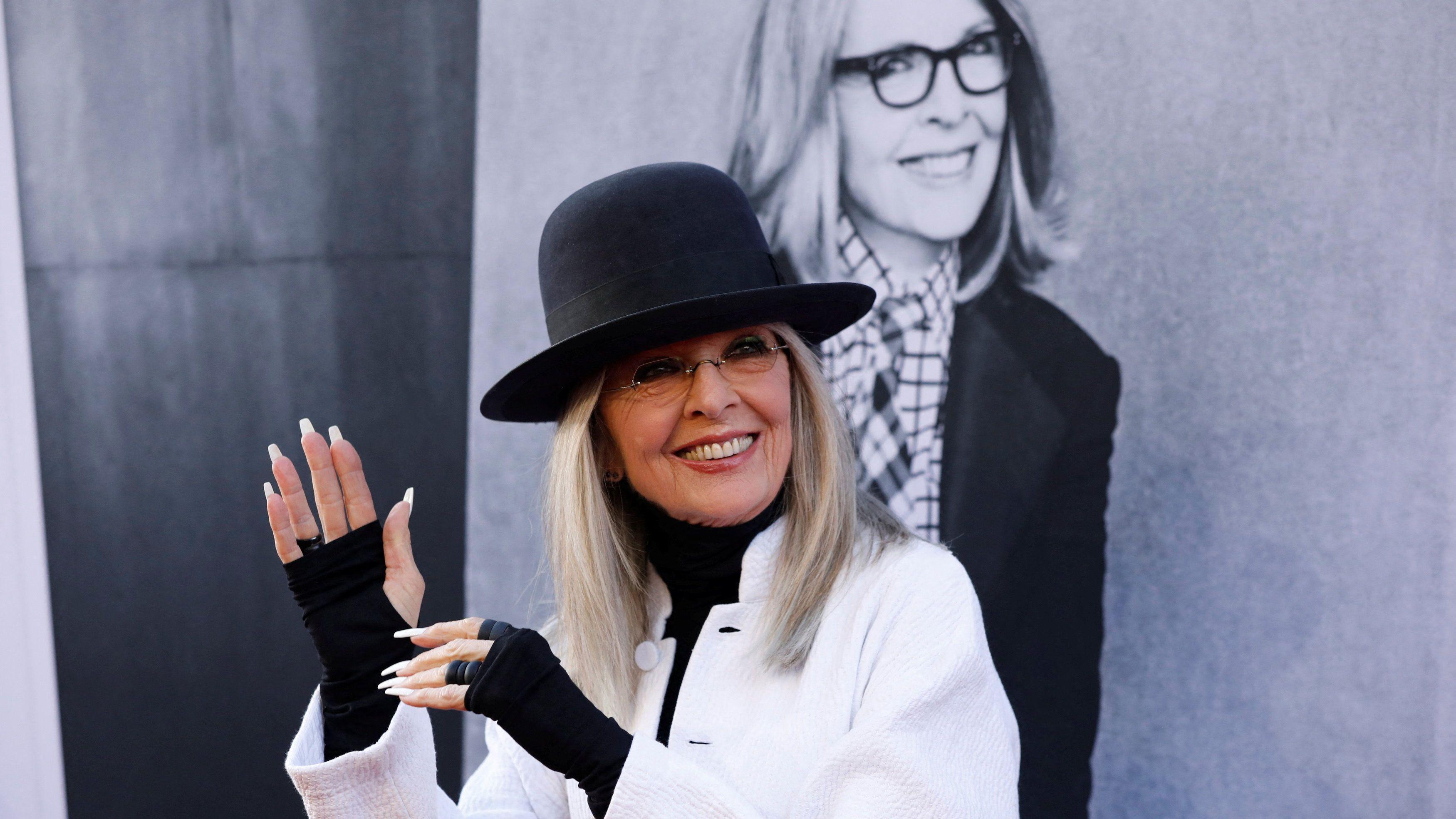 'Ikona stila, humora i komedije': Preminula glumica Dajana Kiton 1 Dajen Kiton ima crni šešir na glavi smeje se i nosi beli kaput. Pokazuje ruke na kojima ima crne rukavice bez prstiju