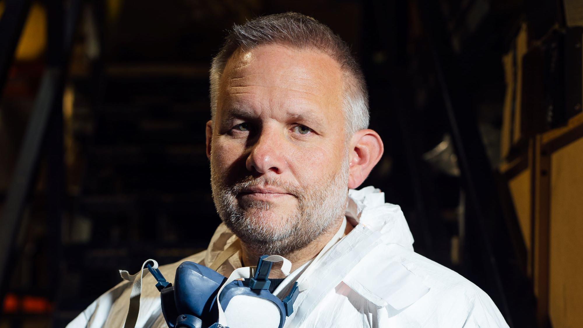 'Počeo sam kao perač prozora, a sada čistim mesta zločina' 2 Fotografija Bena Džajlsa izbliza. Ima 49 godina, kratku sedu kosu. Nosi masku za lice oko vrata. Nosi zaštitnu opremu oko vrata, belo odelo sa kapuljačom