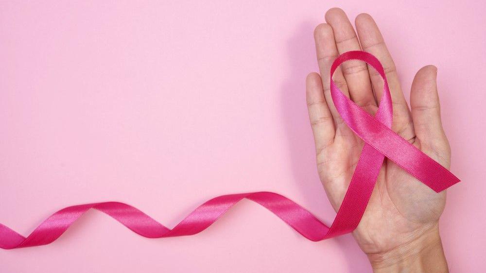 Kampanja za borbu protiv raka dojke sa ružičastom trakom, Žena drži ružičastu traku na ružičastoj pozadini. 