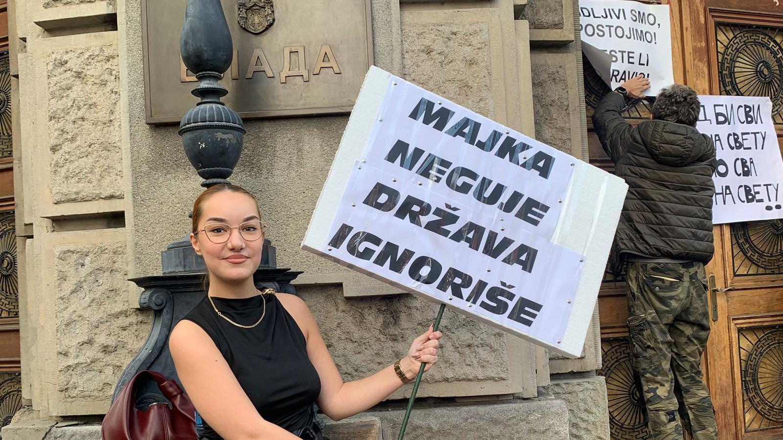 Devojka drži transparent ispred zgrade Vlade Srbije