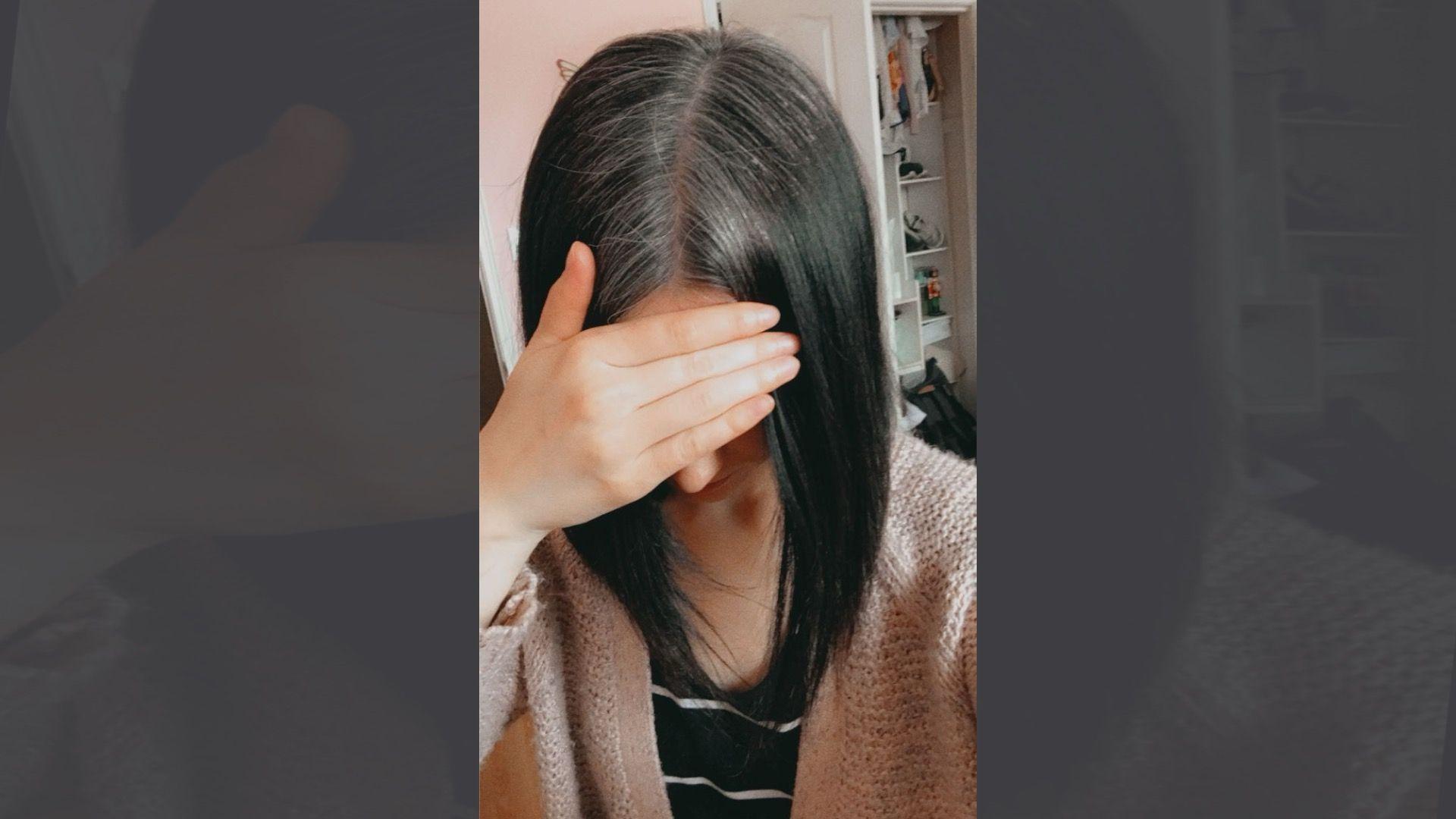 Ešli Šukru prekriva lice rukom dok pokazuje tamnu, pravu kosu do ramena, koja je u korenu seda