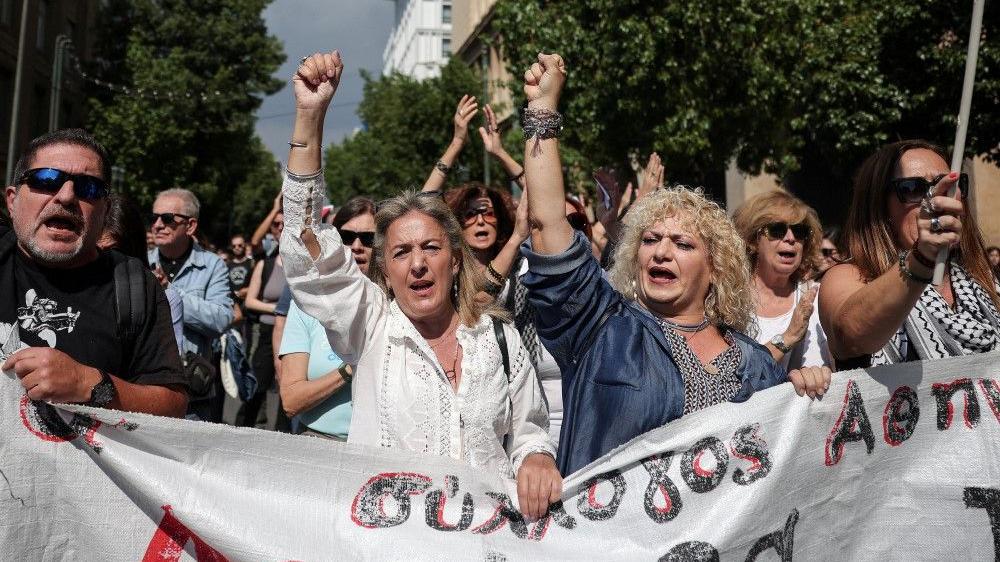 Štrajk u Grčkoj: 'Nećemo da nam radni dan traje 13 sati' 1 žene sa uzdignutim pesnicama u Grčkoj, štrajk radnika u Grčkoj, Jednodnevni štrajk radnika u Grčkoj zbog vladinog predloga da poslodavci mogu da produže radno vreme do 13 sati