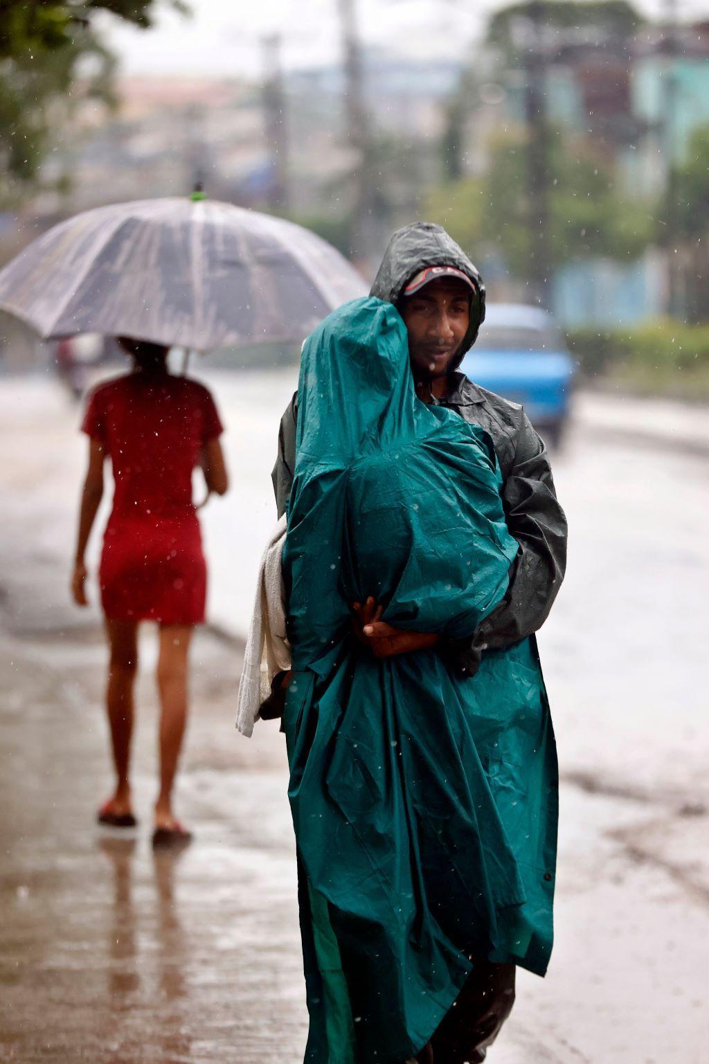 Uragan Melisa: Desetine mrtvih na Karibima 10 muškarac nosi dete dok pada kiše, oboje su u kabanicama, uragan, uragan melisa