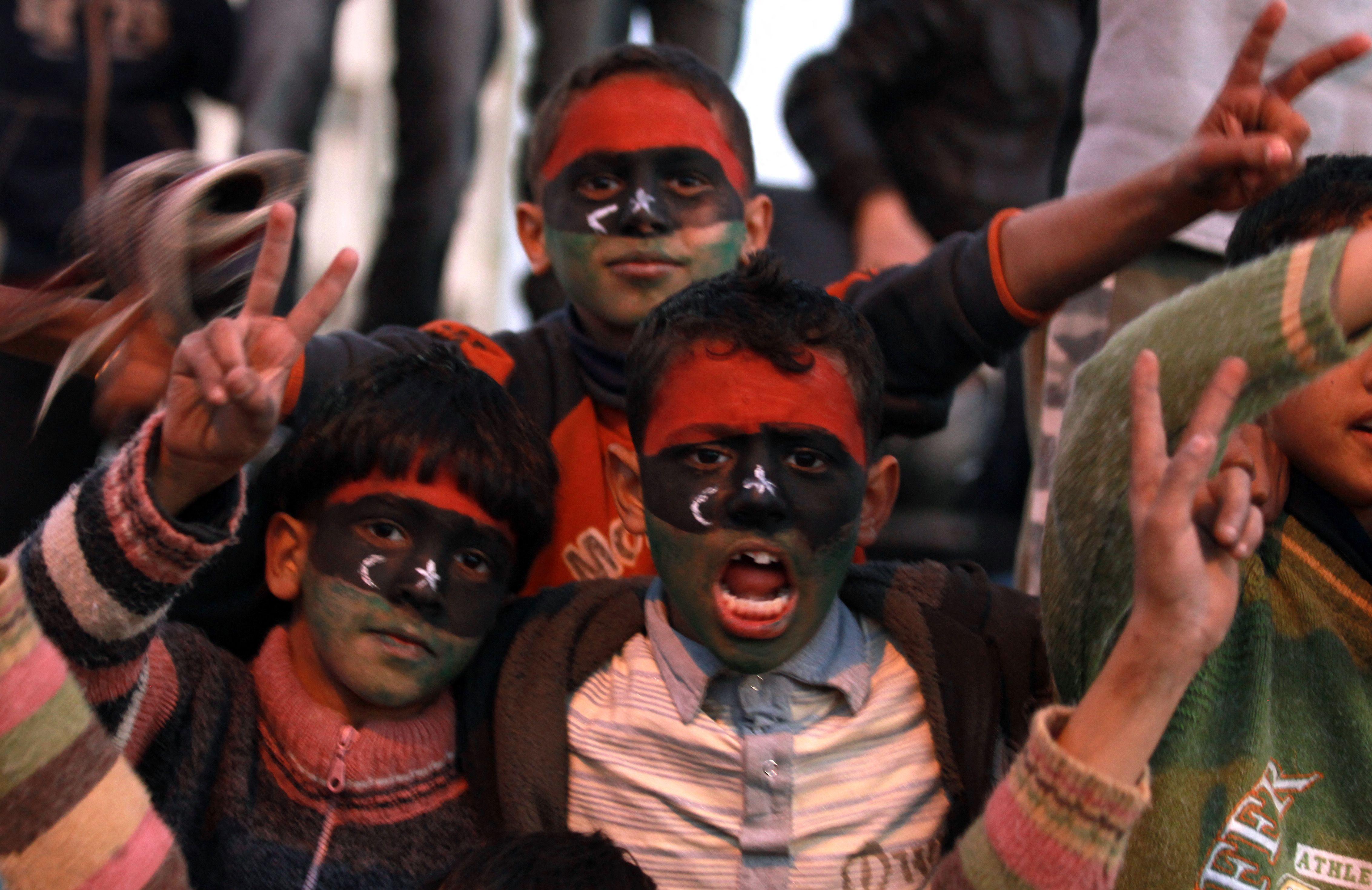 Children with their faces painted in the colours of their old national flag, hold the hands up in the V-for-victory position. A boy has his mouth open and is shouting.