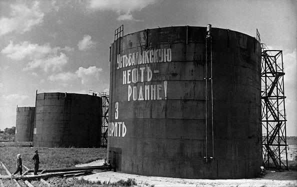 Može li jeftina nafta da pomogne Trampu u Ukrajini, kao nekad Zapadu u Hladnom ratu 3 Crno-bela fotografija prikazuje dvoje ljudi koji čitaju slogan 'Nafta za otadžbinu' na velikim rezervoarima nafte u Sibiru u avgustu 1965.