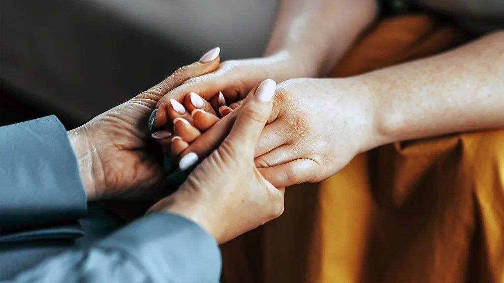 dve žene se drže za ruke, a lica im se ne vide 