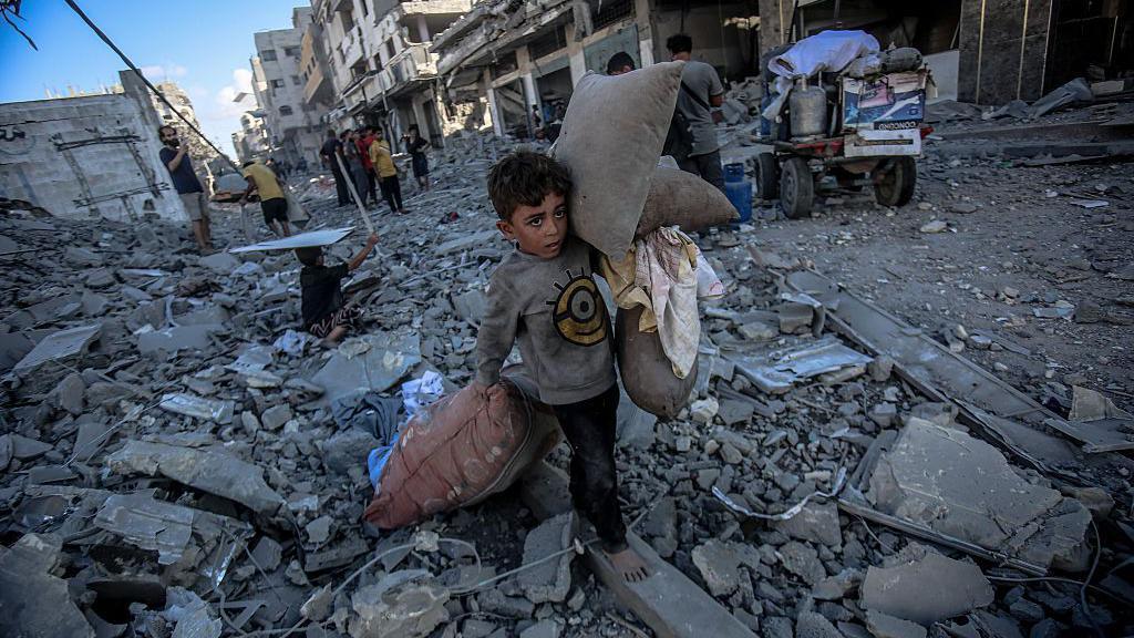 Dete u Gazi nosi jastuke dok hoda po ruševinama