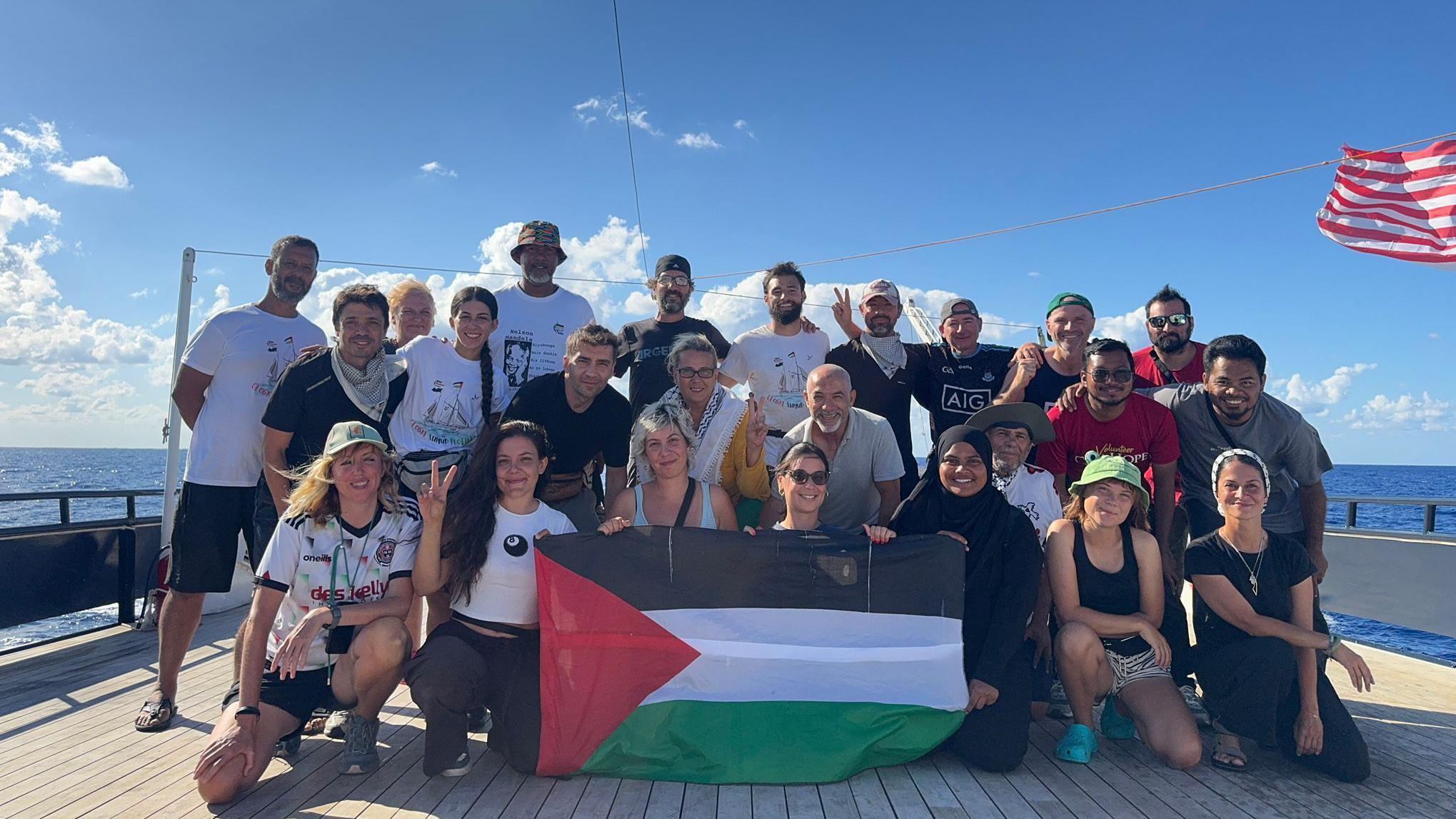 Šta je Sumud flotila i zašto je htela da dostavi pomoć Gazi morem kad Izrael ne da 2 Grupa od oko 25 ljudi pravi selfi na palubi broda po sunčanom danu. Obučeni su ležerno i deluju srećno, osmehujući se kameri. Drže palestinsku zastavu, a nekoliko njih podiže ruke u znaku „v kao pobeda“. Crveno-bela zastava se vidi kako se vijori na vetru desno od slike.