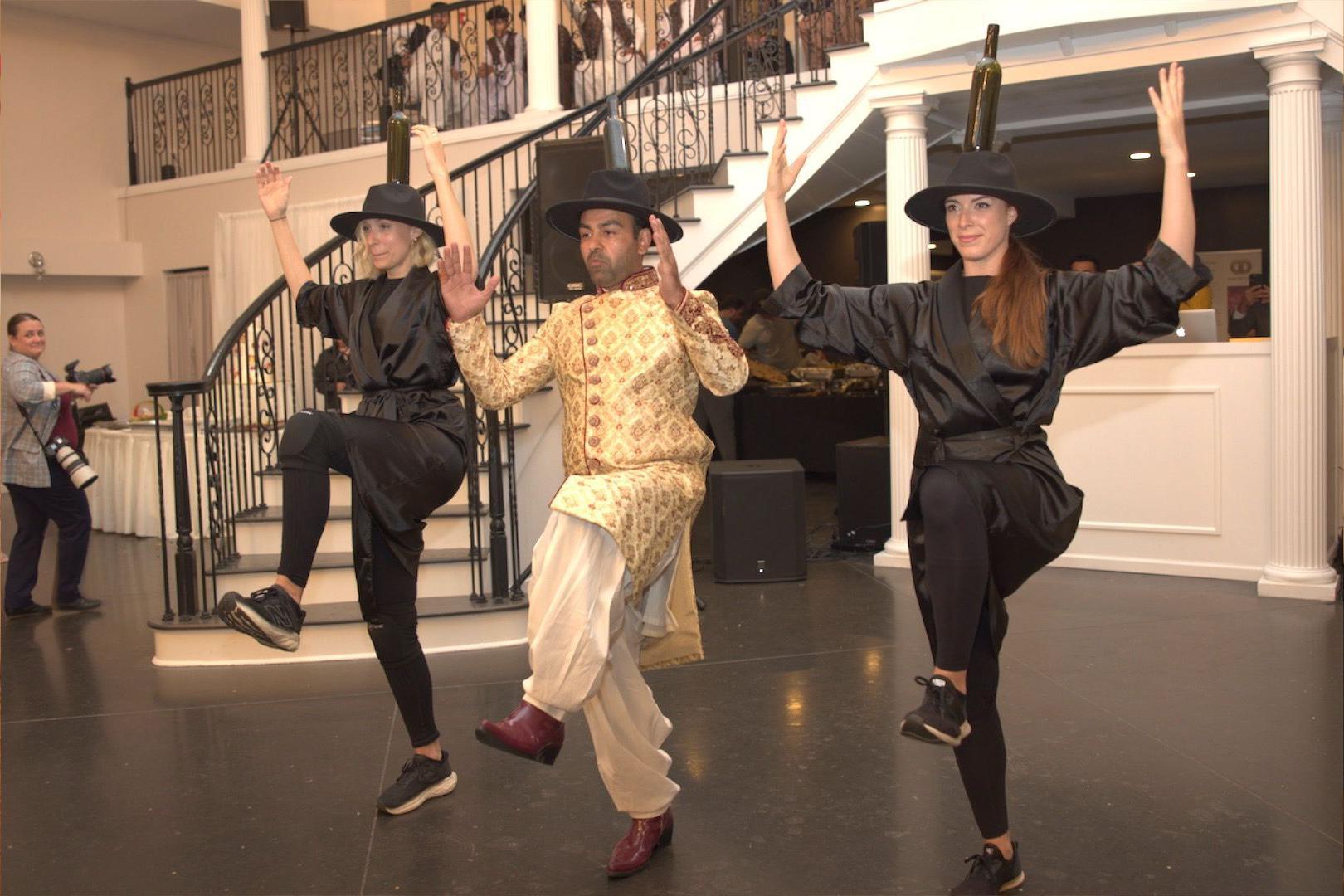 Safi i Sami plešu zajedno sa još jednom ženom. Svo troje nose velike šešire na čijem vrhu je flaša 