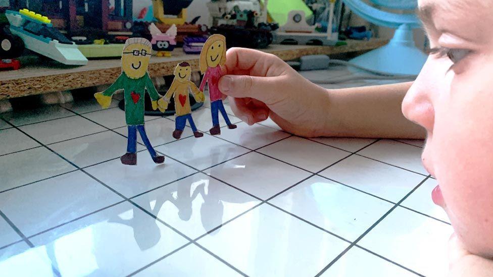 ilustracija - dete drži od kartona napravljenu porodicu