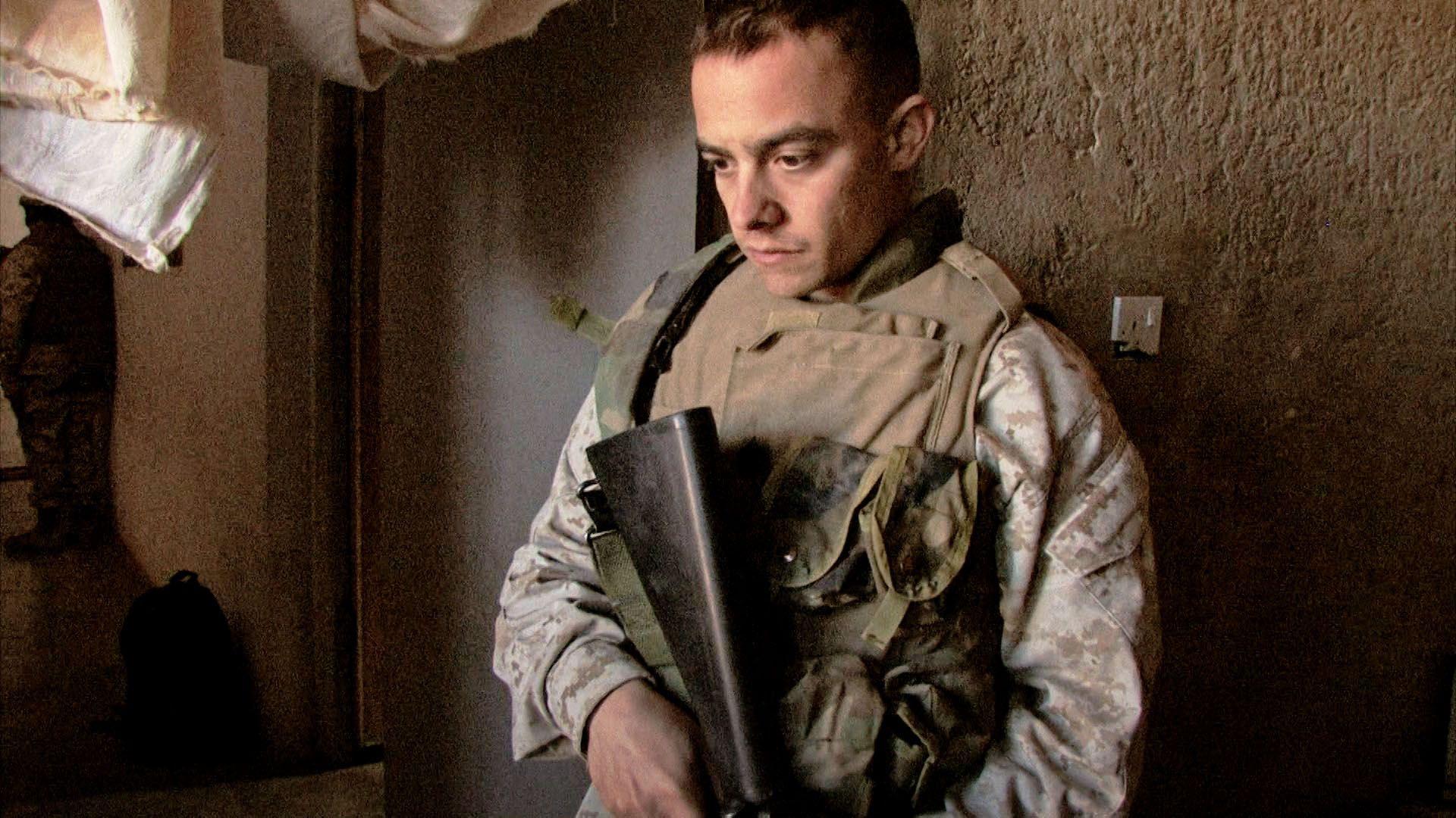 muškarac u vojnoj odeći sa puškom gleda u pod 