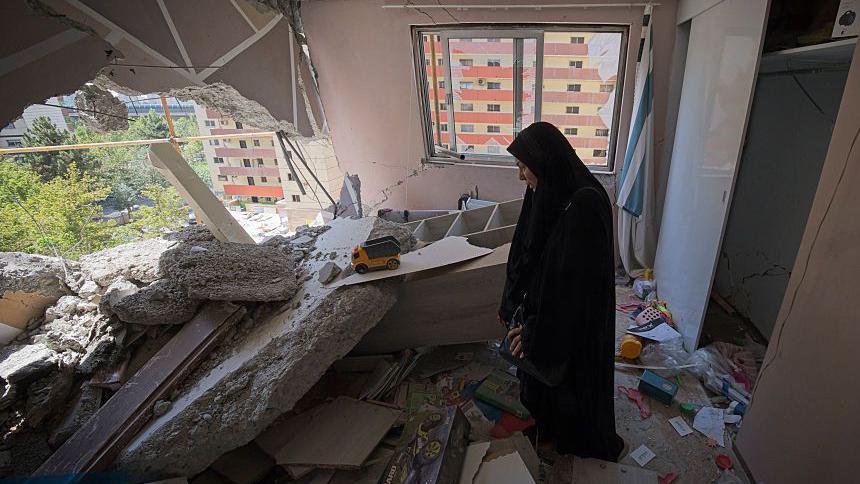 Žena stoji u razrušenom stanu 