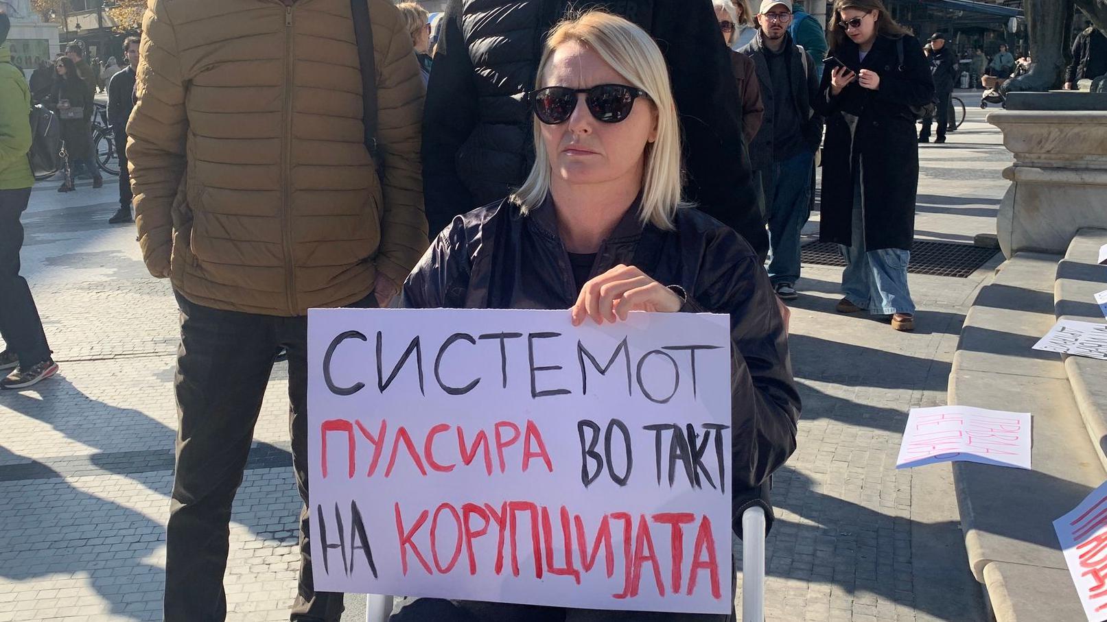 Žena u invalidskim kolicima drži transparent sa natpisom - Sistem pulsira u ritmu korupcije