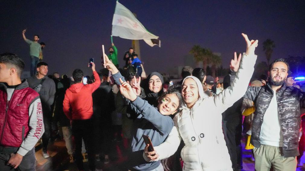 žena i dete se osmehuju i mašu, pokazujući rukama pobedu u Damasku 9. decembra 2024. 