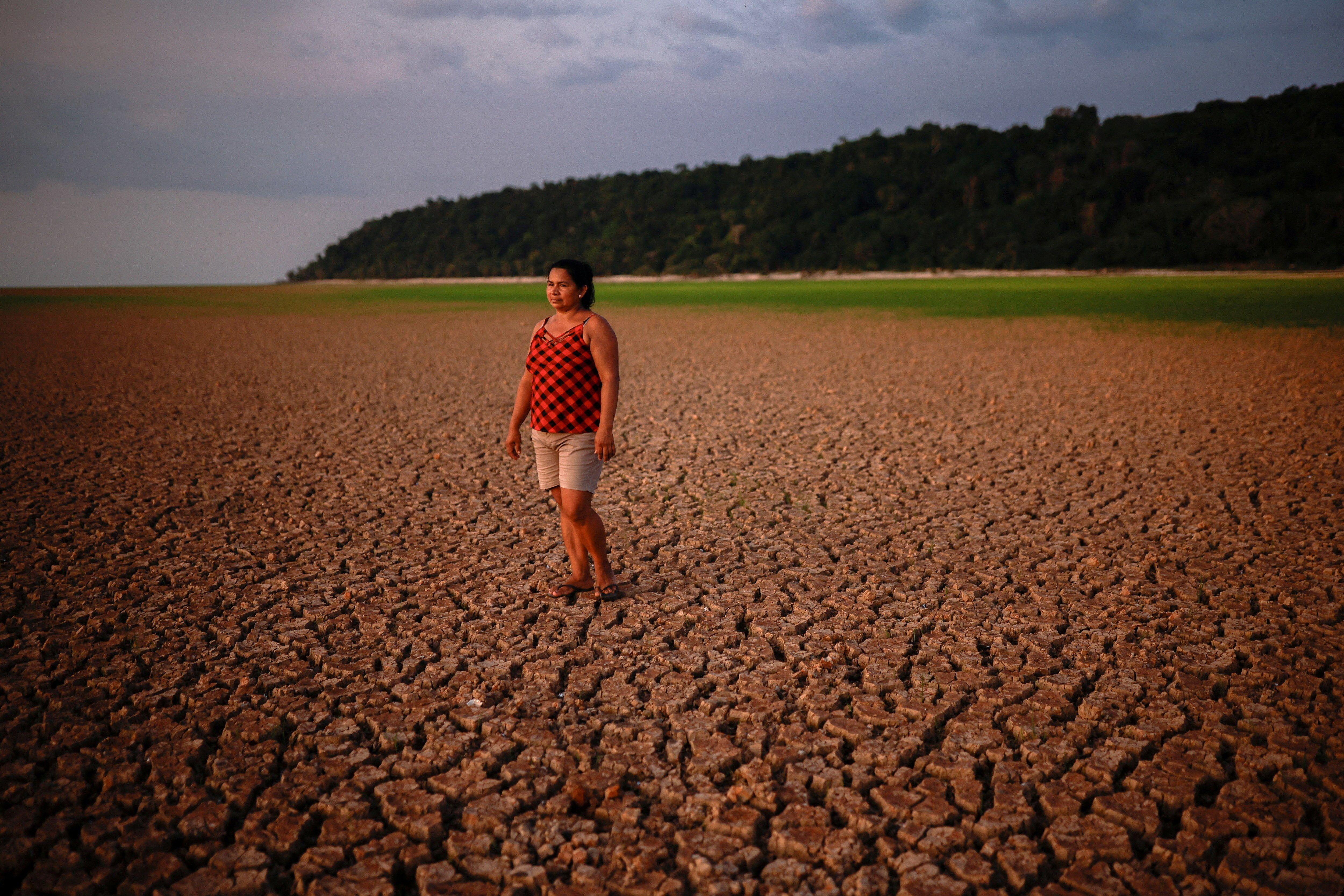 žena stoji na isušenom i ispucalom rečnom koritu dok se u daljini nazire voda 