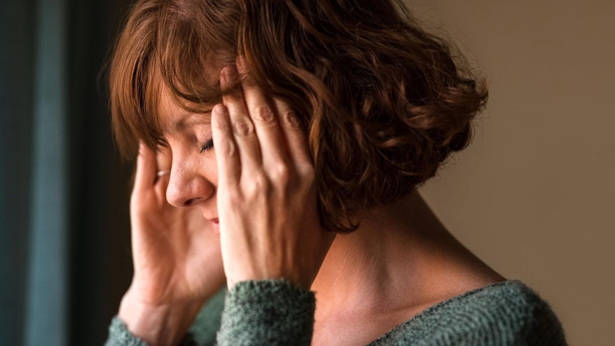 Žena srednjih godina drži se za glavu
