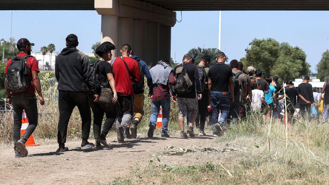 Kolona ljudi, mahom muškaraca prolazi ispod mosta 