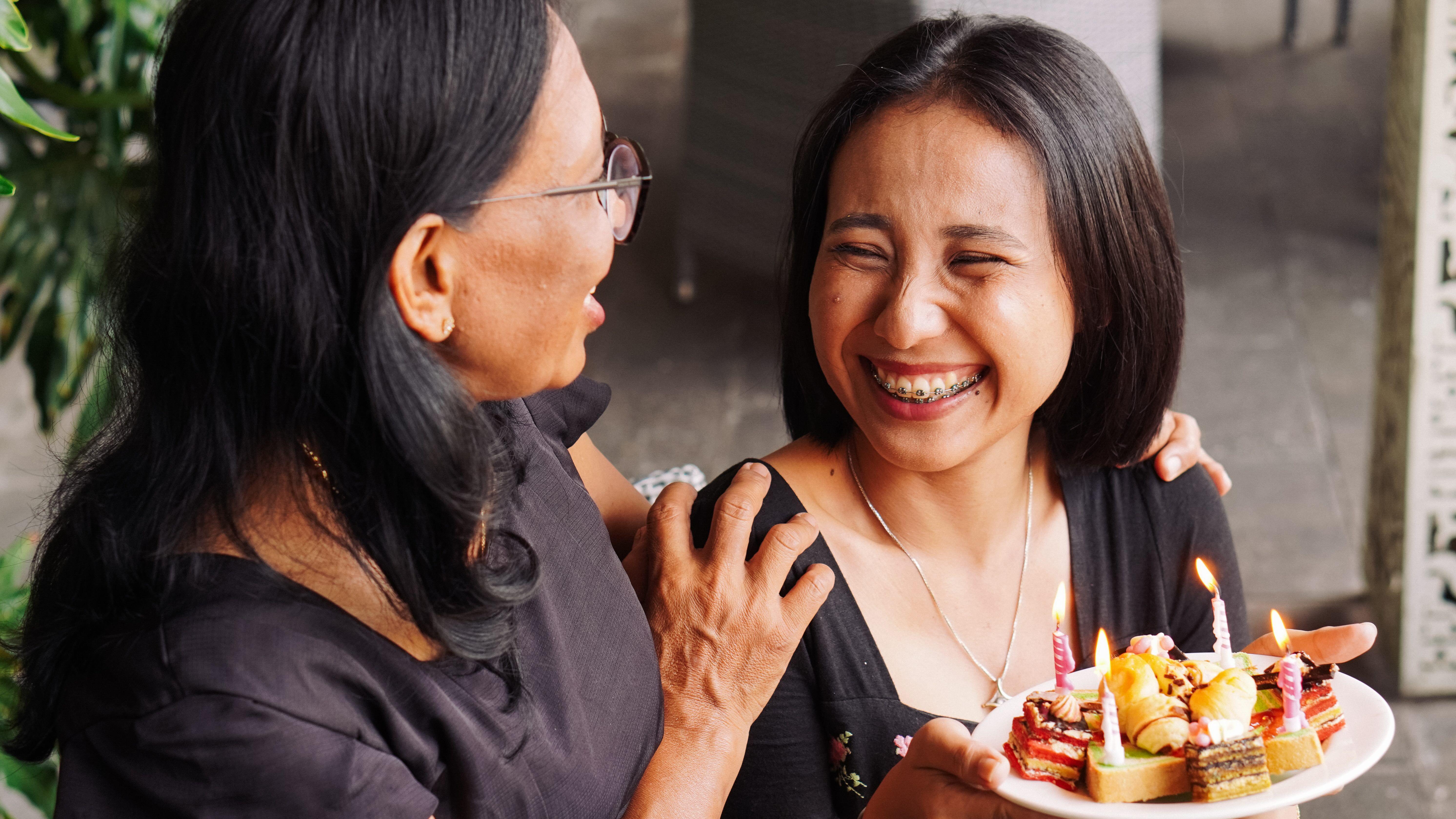 Две жени се смешкаат, додека едната држи чинија со колачи и свеќи