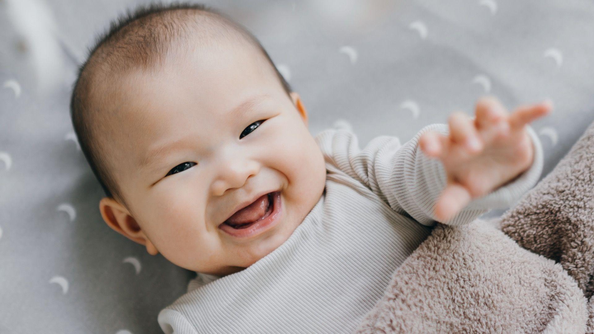 Бебето лежи во кревет и се смешка на камерата