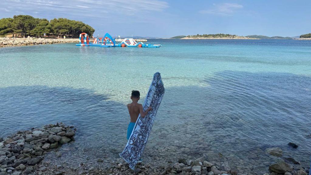 dečak sa dušekom na naduvavanja u plićaku na moru stoji slikan s leđa