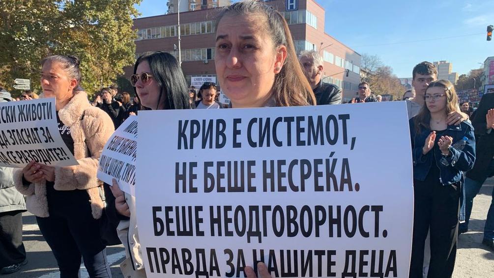 Žena drži beli papir na kojem je ispisano - Kriv je sistem, nije nesrećni slučaj. To je bila neodgovornost. Pravda za našu decu.