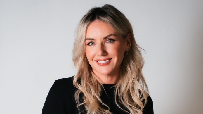 Sali Hjuz u crnoj bluzi, puštene plave kose, nasmejana pozira