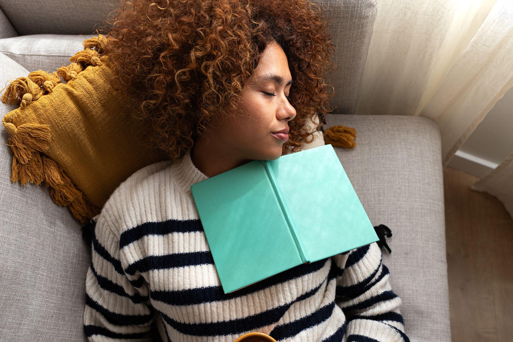 žena sa kovrdžavom kosom spava na krevetu, a preko nje je otvorena knjiga