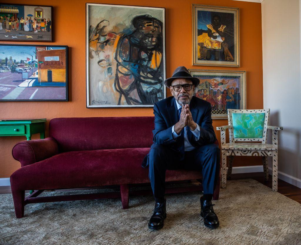 Antonio Salazar-Hobson sedi na sofi, stariji čovek u odelu i sa šeširom sedi na sofi i gleda u kameru