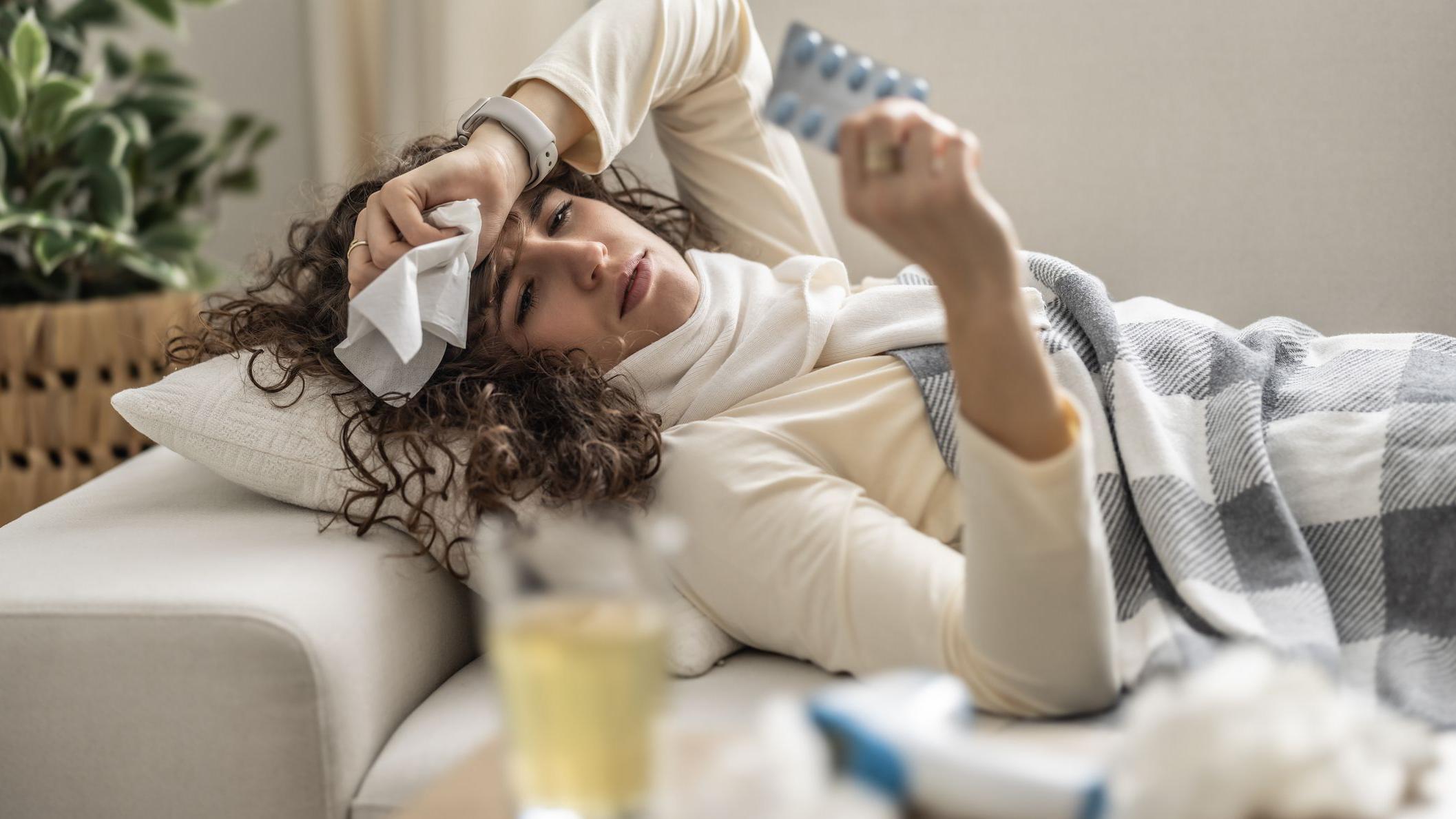 Mlada žena leži bolesna na kauču, držeći pakovanje antibiotika  