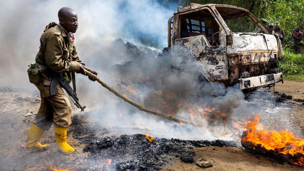 Vojnici kongoanske vojske i trupe UN pregledaju mesto islamističkog napada u aprilu 2021. godine. Vidi se vatrogasac kako se bori sa plamenom.