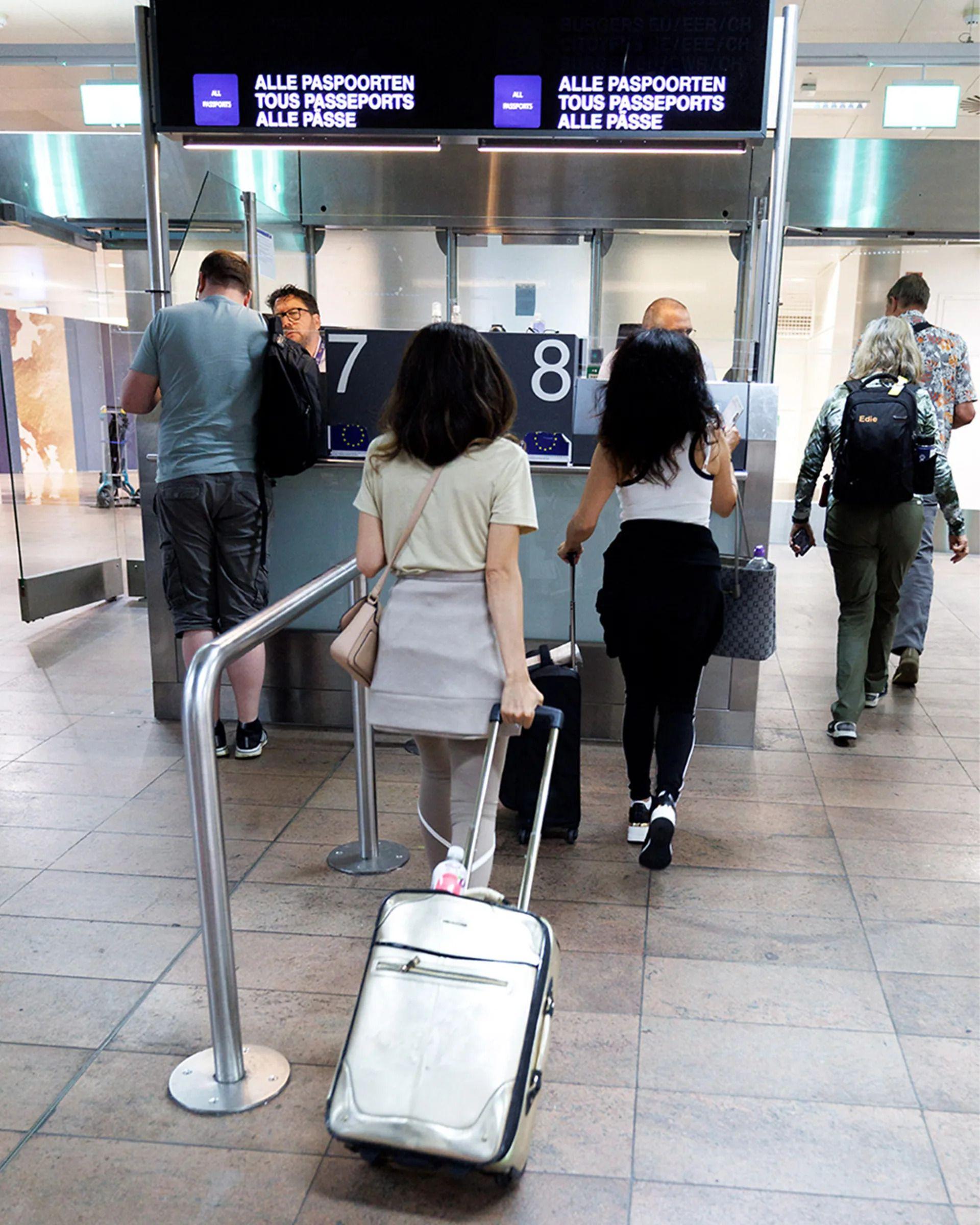 Pasoška kontrola na aerodromu i nekoliko putnika sa koferima 