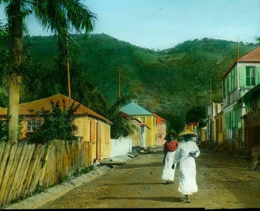 Kako je Danska prodala Devičanska Ostrva Americi i ima li to veze sa Grenlandom 3 Dve žene sa širokim šeširima i belim suknjama šetaju ulicom sa šarenim kućama u Sent Tomasu na Američkim Devičanskim Ostrvima, na slici iz oko 1890. godine