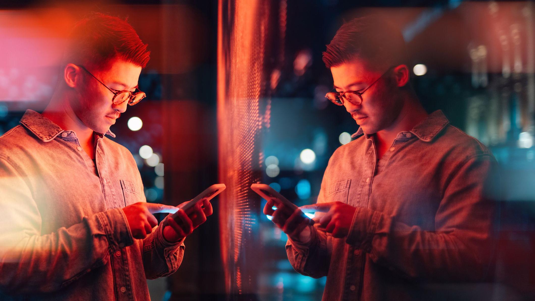 Muškarac sa telefonom u rukama, stoji ispred ogledala. 