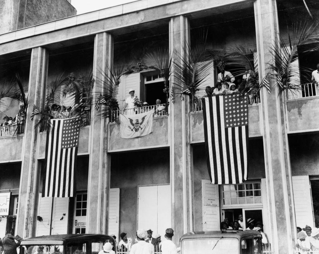 Kako je Danska prodala Devičanska Ostrva Americi i ima li to veze sa Grenlandom 5 Crno-bela fotografija fasade zgrade Svetog Tome sa velikim američkim zastavama koje vise sa njenih balkona. Eleonor Ruzvelt, tada prva dama SAD, je na jednom od balkona, na slici iz 1934. godine.
