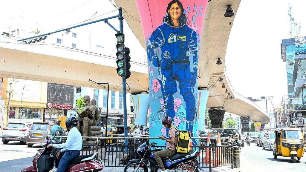 Umesto nekoliko dana, 'zaglavila' devet meseci u svemiru: Priča hrabre astronautkinje 2 Veliki mural sa likom Sunite Vilijams u plavom svemirskom odelu na stubu jedne od saobraćajnih raskrsnica kuda prolaze motociklisti, automobili i tuk tukovi