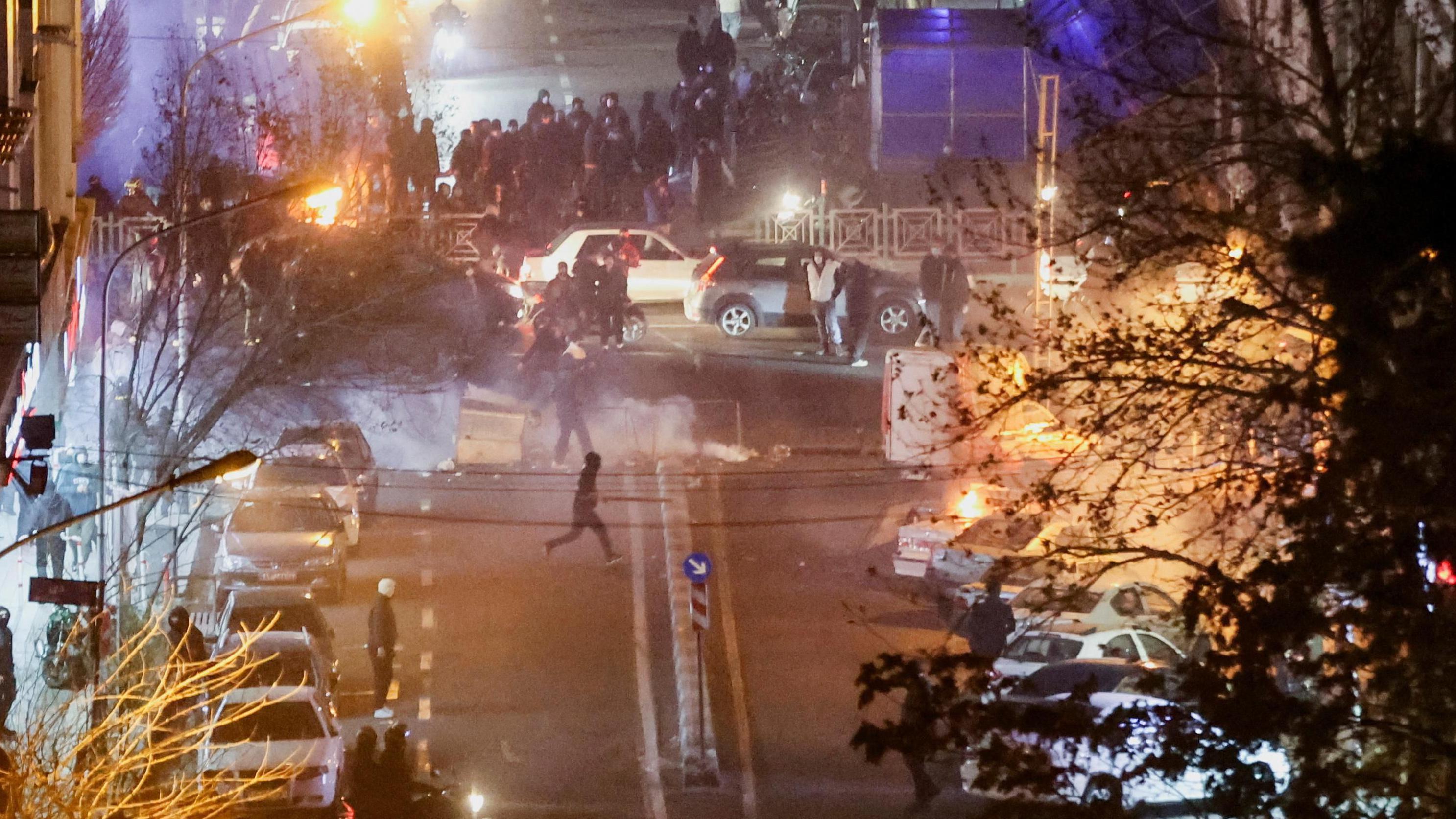 protesti u iranu, iran, demonstranti u Iranu oko parkiranih automobila na ulici. Vidi se dim, a u blizini gori vatra