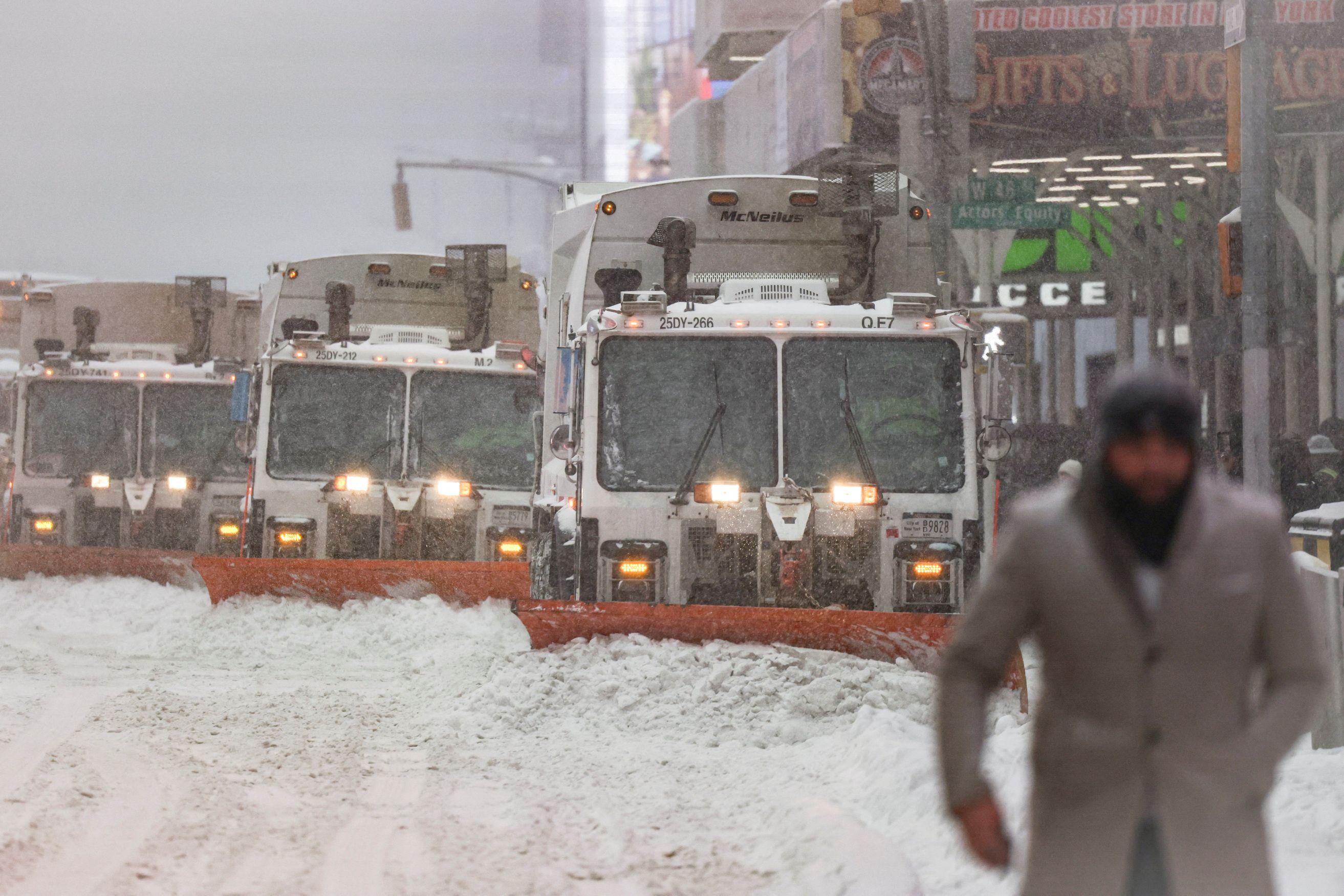 Snežna oluja paralisala Ameriku: Najmanje sedmoro mrtvih, stotine hiljada bez struje 7 U prvom planu muškarac sa kapom i šalom u sivom kaputu, u drugom planu kamioni koji čiste sneg sa ulice