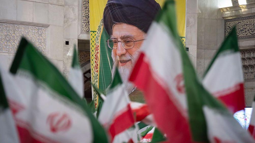 Iranske zastave u prvom planu sa posterom koji prikazuje iranskog vrhovnog vođu Alija Hamneija u pozadini