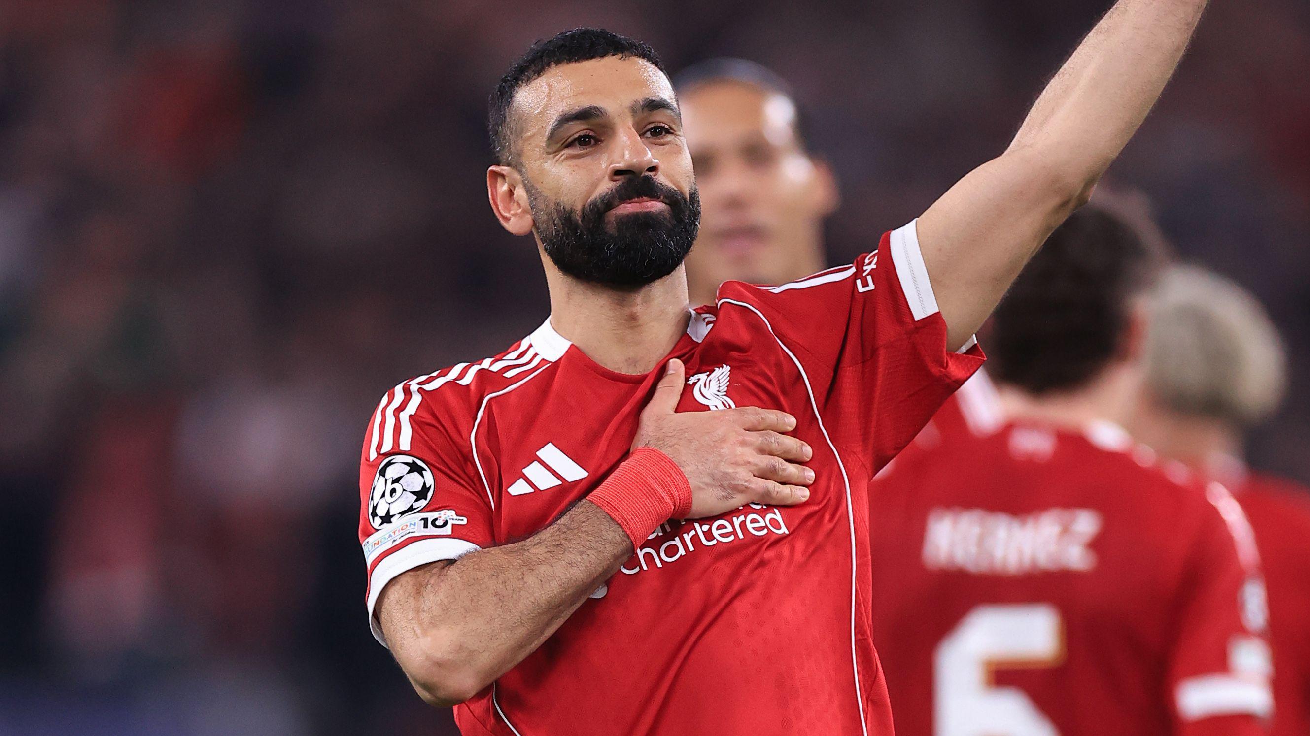 Napadač Liverpula Mohamed Salah maše navijačima dok jednom rukom dok drži grb Liverpula

