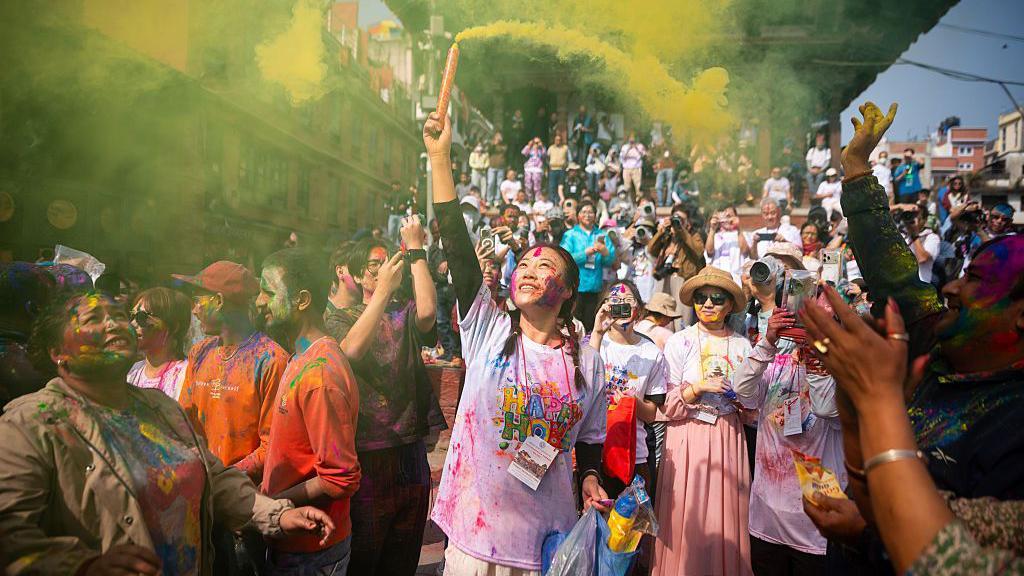 Prolećni festival šarenila i plesa na ulicama Indije 10 Žena namazana prahom po licu ispaljuje dimnu bombu tokom proslave festivala, a oko je nekoliko ljudi