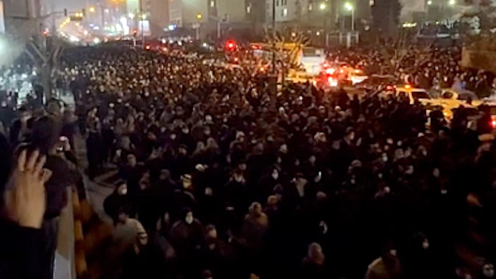 Ajatolah Hamnei: Kako je iranski vrhovni vođa držao vlast čeličnim stiskom 14 A view from a balcony at night of a street filled with people, stretching into the distance, marching towards the camera on 8 January 2026. The road is lit by streetlights, car headlights and lights from buildings. To the left is a balcony where people are watching. A woman nearby is clapping.