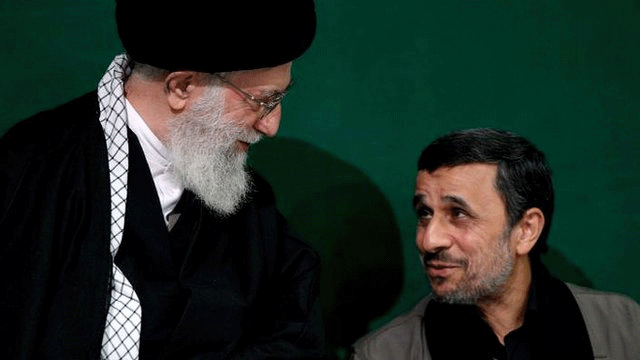 Ajatolah Hamnei: Kako je iranski vrhovni vođa držao vlast čeličnim stiskom 19 Khamenei looking downwards at Ahmadinejad, who is talking and appearing to be partially smiling. Khamenei is wearing a traditional black robe and black head covering. Ahmadinejad has a black open-necked shirt, a light grey jacket and no head covering. He has a thin grey beard and black hair that is partially grey.