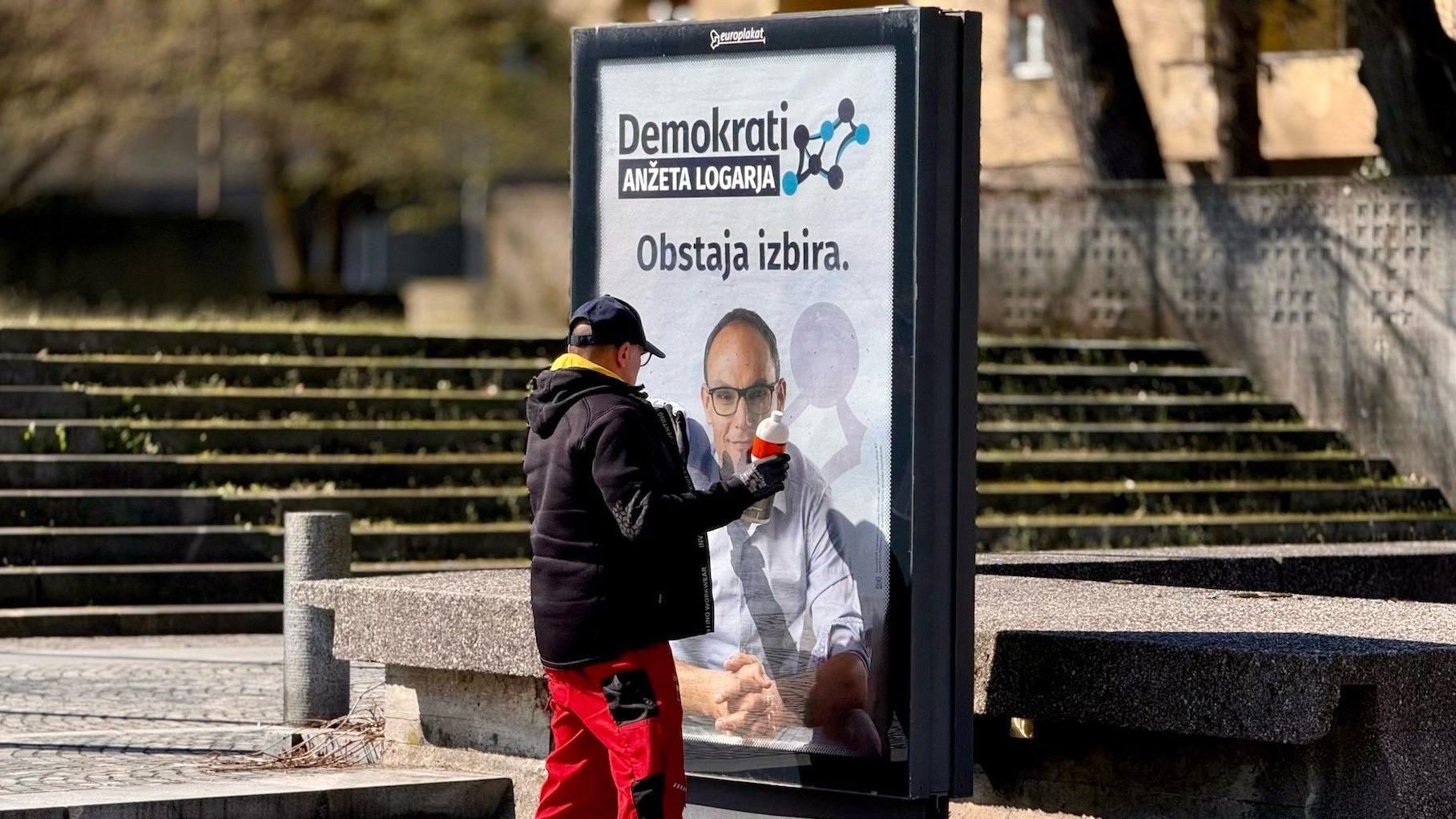Izbori u Sloveniji: Kratak put od političkog punoletstva do 'najveće afere od osamostaljenja' 1 Čovek čisti bilbord sa pozivom na glasanje Demokratske partije