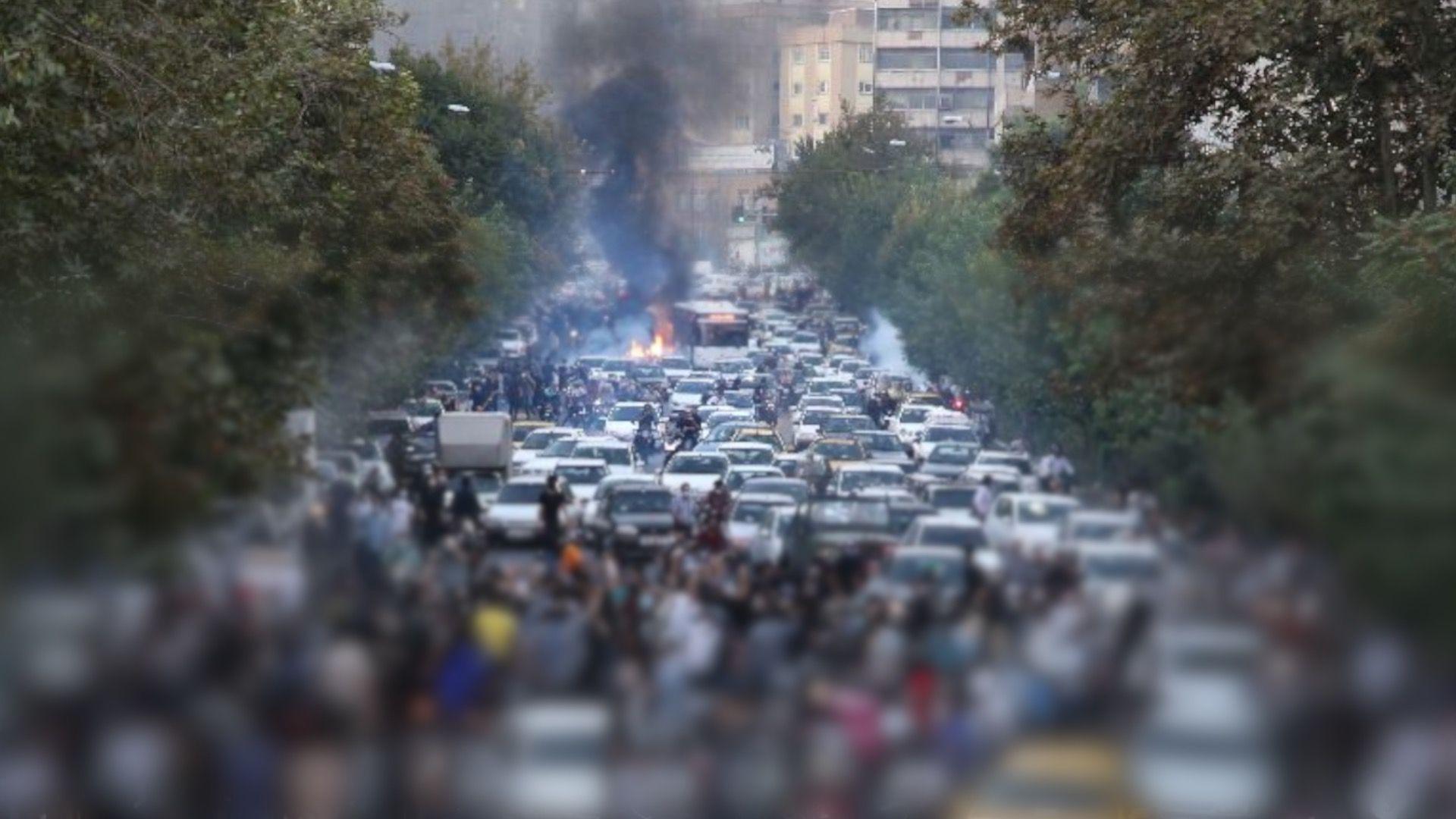 Ajatolah Hamnei: Kako je iranski vrhovni vođa držao vlast čeličnim stiskom 13 A wide street in Tehran blocked by vehicles, including cars and motorcycles, during the daytime on 21 September 2022. Dozens of people are gathered in front of and among the vehicles. A blur imposed by the BBC conceals the identities of people in the lower part of the image and nobody can be identified in the shot. A fire is burning in the background, with flames and dark black smoke billowing into the air. Green trees line both sides of the street. Tall buildings are in the background.