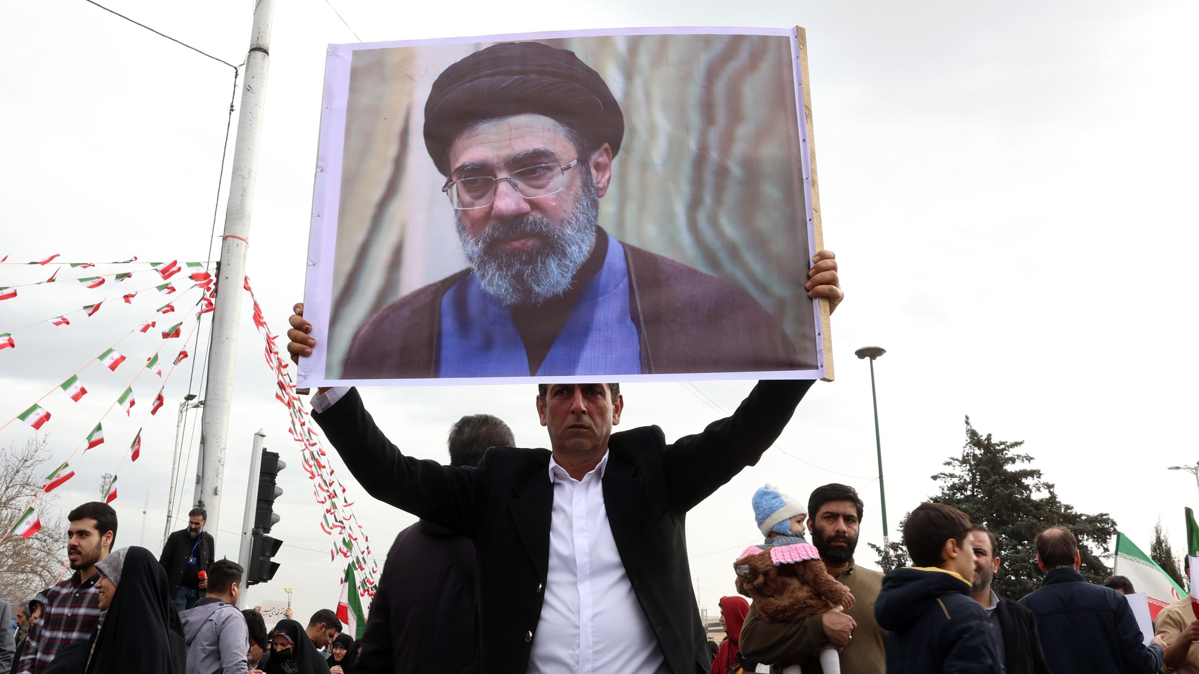 Ko je Modžtaba Hamnei, novi vrhovni vođa Irana 2 Iranac, u crnom sakou i beloj košulji, drži sliku Modžtabe Hamneija, dok učestvuje u proslavi 47. godišnjice Islamske revolucije u Teheranu 11. februara 2026. godine.