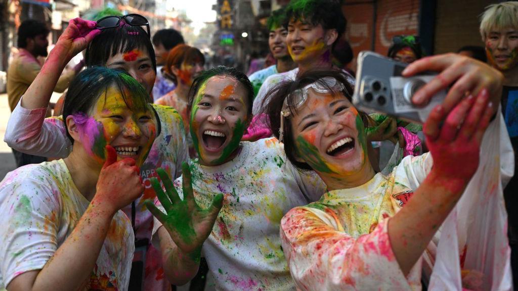 Prolećni festival šarenila i plesa na ulicama Indije 12 Japanski turisti se slikaju, lica su im obojena i nasmejana