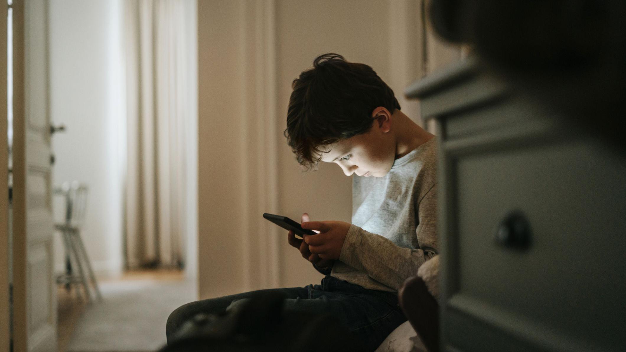 Ne paničite - pet načina da smanjite beskrajno skrolovanje vaše dece 1 Dečak gleda u ekran mobilnog telefona, sedi na fotelji u sobi, iza komode