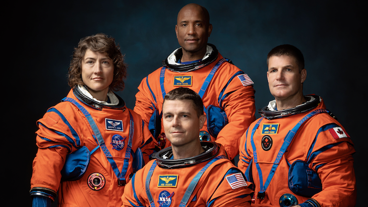 'Mesečeva misija': Ko su astronauti u posadi Artemisa Dva 3 Na slici je četvoro astronauta u jarko narandžastim svemirskim odelima kako poziraju za formalni grupni portret na tamnoj pozadini. Odela su glomazna sa kaiševima i džepovima, što naglašava njihov tehnički dizajn. Troje astronauta stoje, a jedan sedi, svi okrenuti ka kameri.