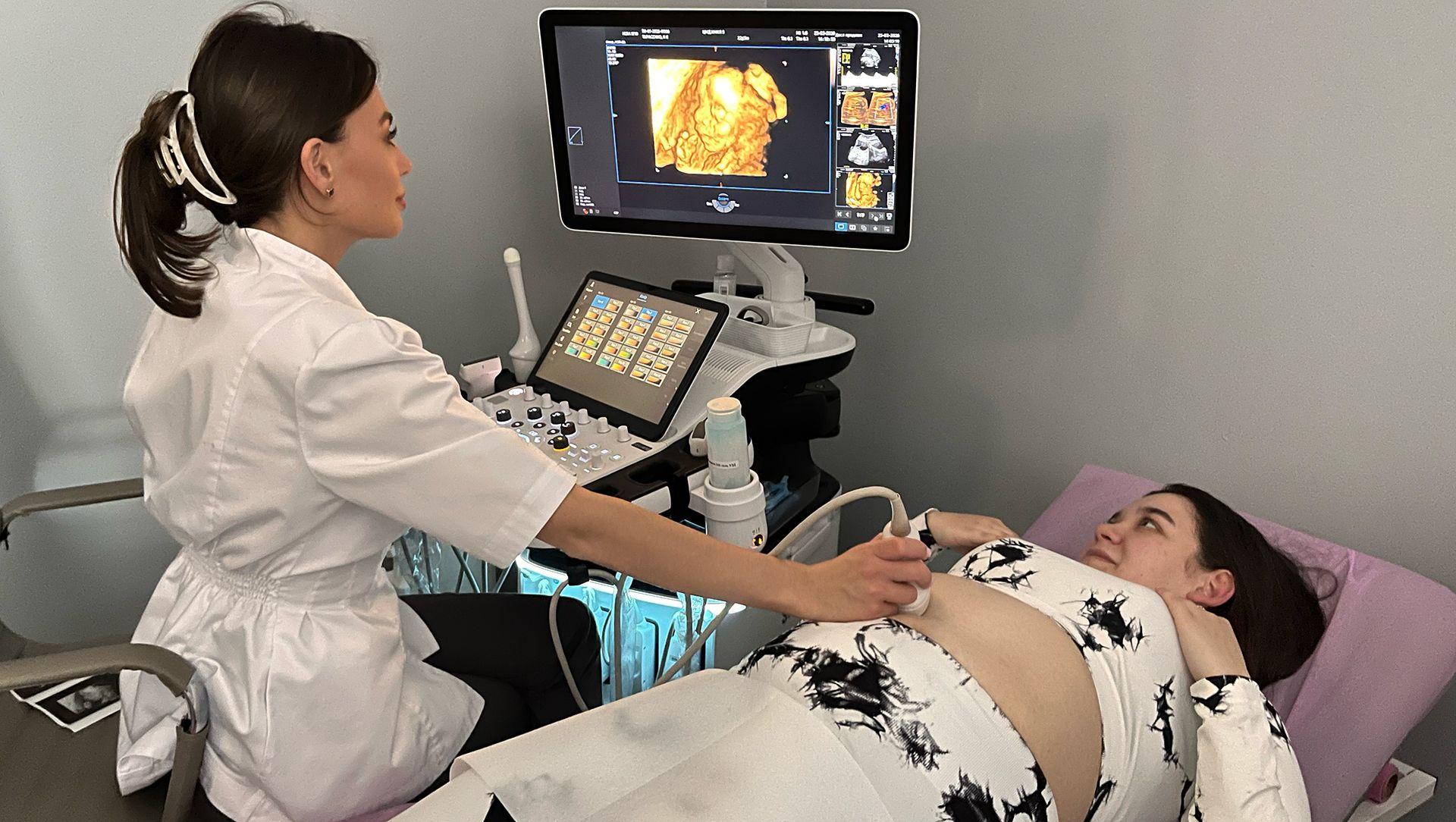 Trudnica leži na krevetu u klinici tokom skeniranja. Žena u belom mantilu, sa dugom, tamnom vezanom kosom, izvodi proceduru. Obe gledaju u ekran na kojem se vidi fetus.